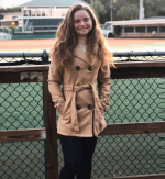 Student with long hair smiling and leaning against fence